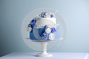 Beautiful two tiered white and blue wedding cake decorated with flowers sugar roses. Concept of elegant holiday desserts