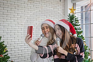 Beautiful two women with santa hat singing karaoke and selfie shooting with smartphone in christmas party