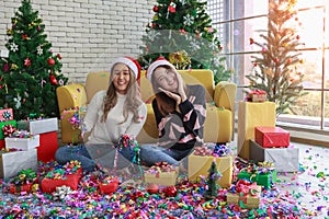 Beautiful two women smiling in falling party popper on floor with flare light at window in christmas party