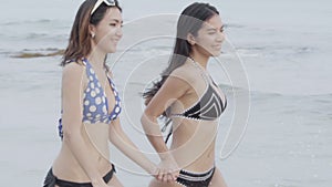 Beautiful two young asian woman in bikini running at the beach, happy girl sexy in summer travel in vacation.