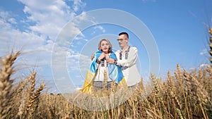 A beautiful Ukrainian couple in embroidered shirts and with a flag in the middle of a wheat field.