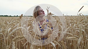 Beautiful Ukrainian woman wearing dress in Ukrainian national flag colours, blue and yellow, at wheat field in morning