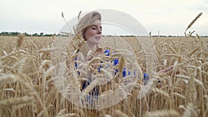 Beautiful Ukrainian woman wearing dress in Ukrainian national flag colours, blue and yellow, at wheat field in morning