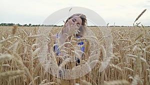 Beautiful Ukrainian woman wearing dress in Ukrainian national flag colours, blue and yellow, at wheat field in morning