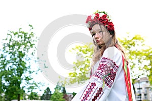 beautiful Ukrainian young woman tender girl in a large red wreath of bright pink white red flowers braiding ribbons in