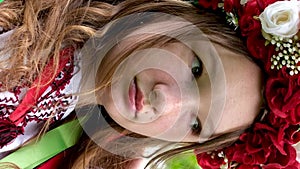 beautiful Ukrainian young woman tender girl in a large red wreath of bright pink white red flowers braiding ribbons in