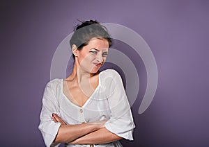 Beautiful unhappy woman in white shirt looking with disgust and grimacing the face on purple background