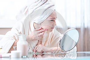 Beautiful unhappy young woman with a towel on her head detects acne on her face. Hygiene and care for the skin