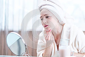 Beautiful unhappy young woman with a towel on her head detects acne on her face. Hygiene and care for the skin