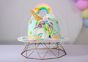 Beautiful unicorn-themed baby girls birthday cake on a stand. Cute unicorn face and the pastel-colored rainbow decoration