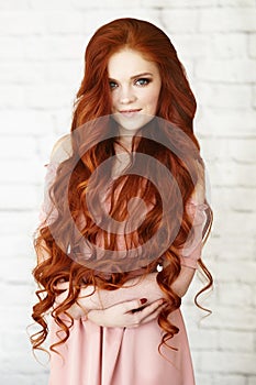 Beautiful unusual woman in pink dress with long red hair on background of brick