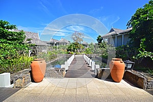 Beautiful upscale resort hotel with small wooden bridge entrance connecting to the villas with two big pots