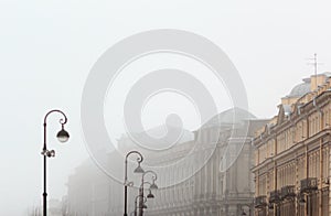 Brutal architecture with columns, stucco and rhythm of windows and lamp posts in foggy day.