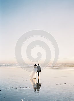 Beautiful vertical back shot of a newly wed couple walking barefoot on the beach