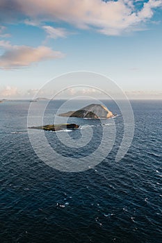 Beautiful vertical shot of small hills in the sea under the cloudy sky during daytime