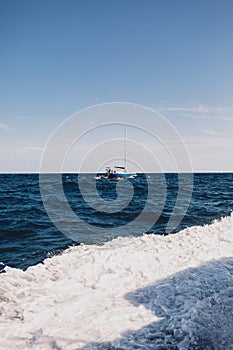 Beautiful vertical shot of the wavy ocean and a ship with the background of blue sky