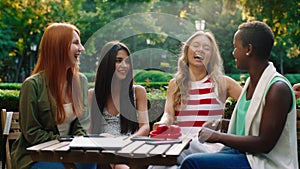 A beautiful and very close friend group of girls are at a park, sitting at a coffee table with all of their things on it