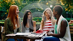 A beautiful and very close friend group of girls are at a park, sitting at a coffee table with all of their things on it