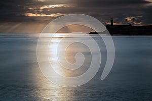 Beautiful vibrant sunrise sky over calm water ocean with lighthouse and harbor wall