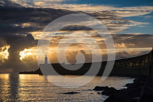 Beautiful vibrant sunrise sky over calm water ocean with lighthouse and harbor wall