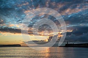 Beautiful vibrant sunrise sky over calm water ocean with lighthouse and harbor wall