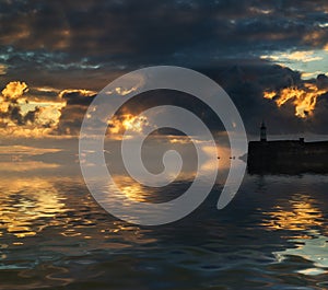 Beautiful vibrant sunrise sky over calm water ocean with lighthouse and harbor wall