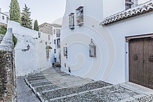 Beautiful view of an alley with houses with white walls, windows with metal lattice, pots with flowers and wooden doors