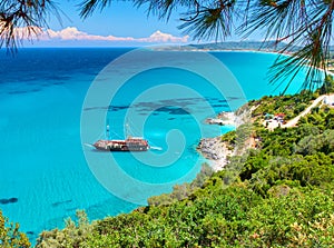 Beautiful view on amazing island bay with pirate corsair style boat ship, swimming people, beach in Ionian Sea blue water, Greece