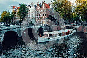 Beautiful view of Amsterdam canals with white cruise boat bridge and typical dutch houses. Holland