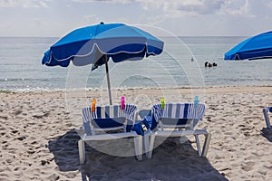 Beautiful view of Atlantic Ocean on sandy Miami Beach with blue sun loungers and umbrellas..