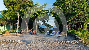 Beautiful view of the beach with chairs under trees and houses in the back in Utila, Honduras