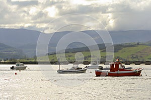 Boats moored in port with the bridge of San Vicende de la barquera, Cantabria, mountains and cloudy sky in the background