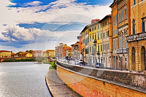 A beautiful view of buildings along the Arno river in Pisa, Italy. A bridge passes over the river and houses on both sides are