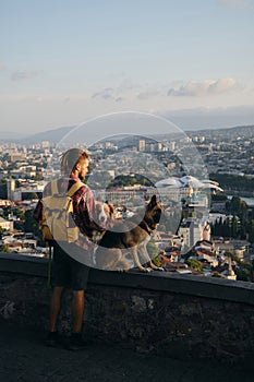 Beautiful view of the capital of Georgia Tbilisi from above from old town. A young man with two dogs admires the sunrise