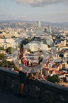 Beautiful view of the capital of Georgia Tbilisi from above from old town. A young man with two dogs admires the sunrise