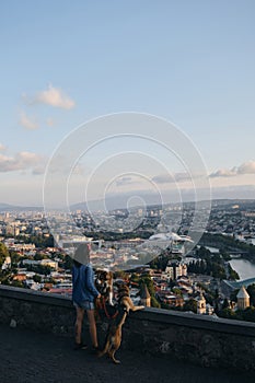 Beautiful view of the capital of Georgia Tbilisi from above from old town. A young woman with two dogs admires the