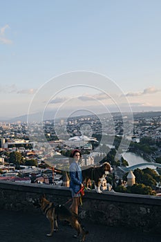 Beautiful view of the capital of Georgia Tbilisi from above from old town. A young woman with two dogs admires the