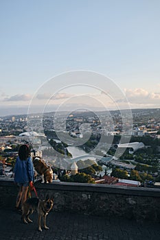 Beautiful view of the capital of Georgia Tbilisi from above from old town. A young woman with two dogs admires the