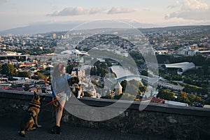 Beautiful view of the capital of Georgia Tbilisi from above from old town. A young woman with two dogs admires the