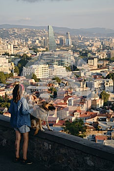 Beautiful view of the capital of Georgia Tbilisi from above from old town. A young woman with two dogs admires the