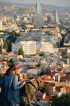 Beautiful view of the capital of Georgia Tbilisi from above from old town. A young woman with two dogs admires the