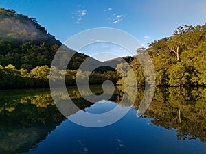 Beautiful view of creek with reflections blue sky, light clouds, fog, mountains and trees on water