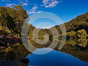 Beautiful view of a creek with reflections of blue sky, light clouds, and trees on water