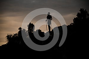 beautiful view of dark silhouette of woman with trekking poles on mountain