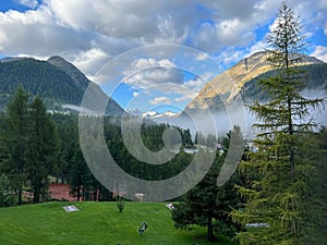 Beautiful view of deep forest with fog over mountains on a cloudy sky day in Pontresina, Switzerland