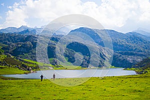 Beautiful view of Ercina Lake in Covadonga Lakes, Asturias, Spain. Green grassland with a couple walking and mountains at the