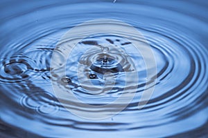 Beautiful view of falling drops on blue water surface isolated on background