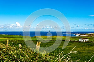 Beautiful view of a field with green grass, the sea and the port of Doolin and the Crab island in the background