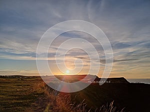 Beautiful view of the green fields and cloudy sky with the shining sun at sunset.