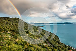 Beautiful view of a green hillside and sea against the background of the cloudy sky with a rainbow.